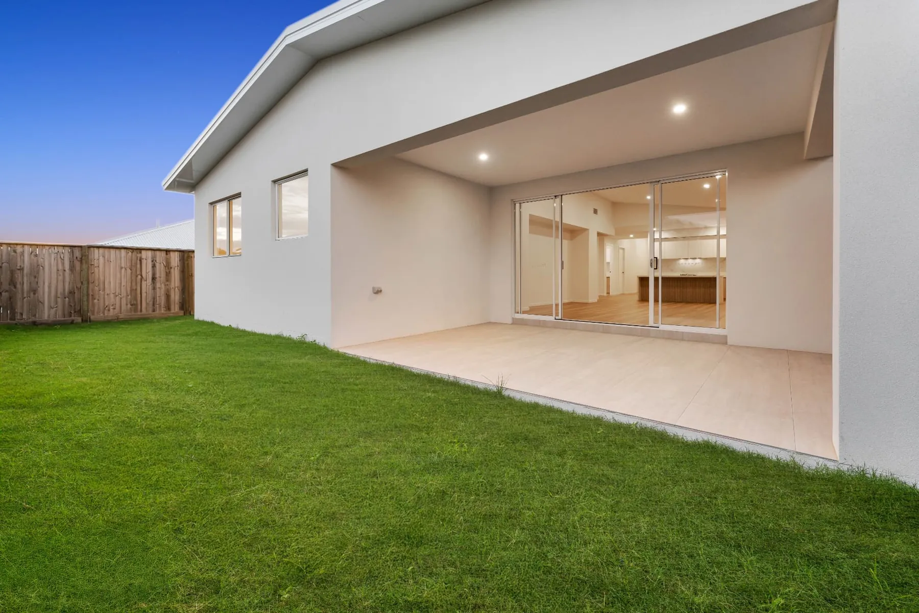 Covered alfresco area opening onto the landscaped rear lawn at dusk