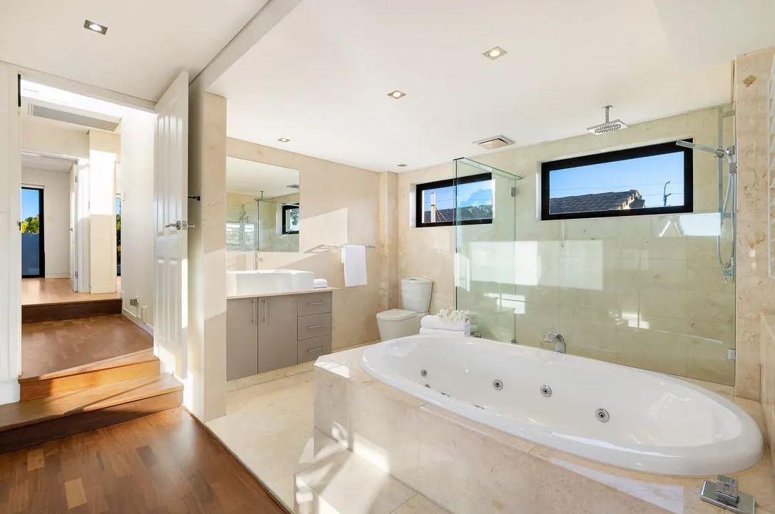 Stone-clad ensuite with spa bath, frameless glass shower and clerestory windows