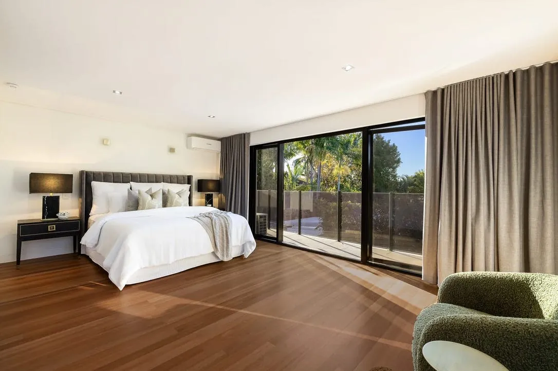Master bedroom with timber floors and full-height glass opening to a balcony